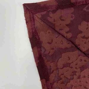 Macro detail of wine red jacquard fabric showing stitching and texture on the evening dress