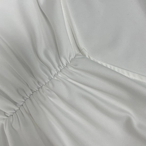 Close-up detail showing white ruched fabric texture and pleated finish of the dress