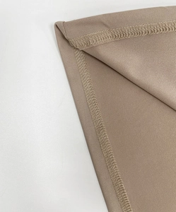Détail des coutures overlock et du tissu lisse sur une robe beige à manches longues