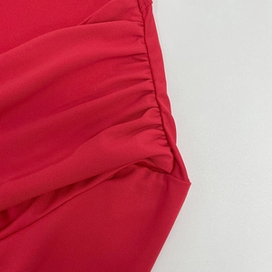 Détail du tissu froncé rouge sur une robe moulante à manches longues et col en V