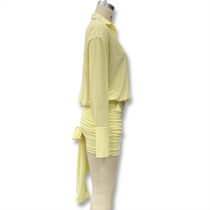 Detail of light yellow shirt dress featuring side ruching and decorative long ribbons