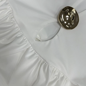 Detail of white dress featuring pleated ruffles and a golden hammered metal button