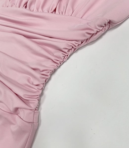 Close-up of light pink ruched knit dress fabric showing soft elastic pleats and texture