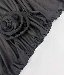 Detail of a 3D fabric rose and ruching texture on a black slim-fit bodycon dress