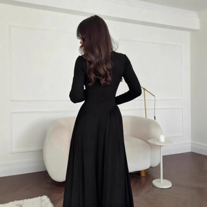 Detail of elegant black long-sleeve dress featuring a cinched waist and pleated flared skirt