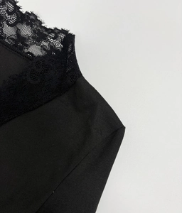Détail de la dentelle délicate sur l'encolure en V d'un haut noir à manches longues