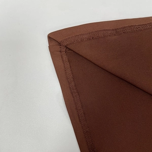 Detailed close-up of brown elastic fabric showing precise machine stitching and overlock edges