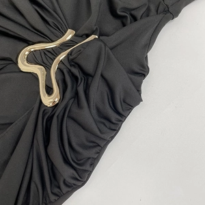 Detailed close-up of pleated black fabric with wave-shaped gold metal buckle detail