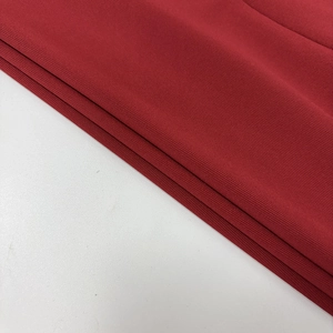 Détail du tissu en maille côtelée rouge avec de fines rayures et un drapé élégant