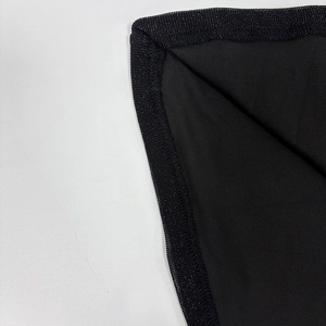 Close-up of industrial overlock stitching on black mesh fabric of the off-shoulder dress