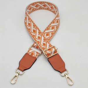 Detail of adjustable orange and white geometric jacquard bag strap with gold metal hooks