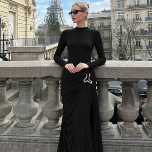 Detail of waist pleats and large gold metallic ornament on a black slim long sleeve dress
