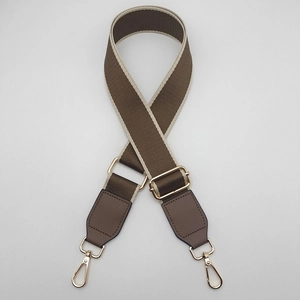 Macro detail of adjustable brown and beige canvas bag strap with gold metal lobster clasps