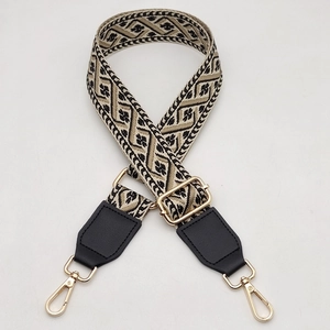 Detail of wide woven strap featuring geometric patterns and golden metal snap hooks