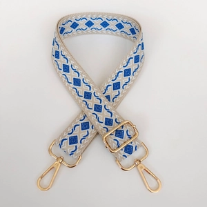 Detail of adjustable woven bag strap with blue geometric diamond pattern and gold metal hooks