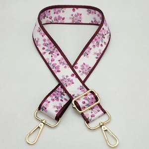 Close-up of adjustable woven bag strap with pink floral pattern and gold metal buckles