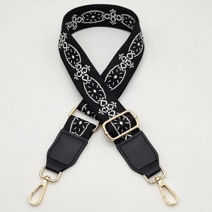 Detailed view of woven black and white ethnic purse strap with gold metal lobster clasps