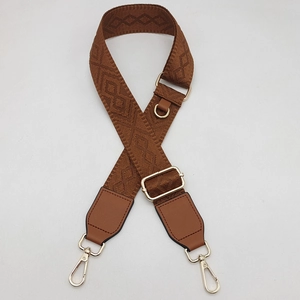 Détail d'une bandoulière marron réglable avec motifs géométriques et boucles dorées