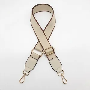 Detail of adjustable beige woven bag strap with brown edges and golden metal hardware