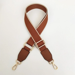 Detail view of brown wide fabric bag strap with golden metal lobster clasps and buckle