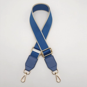 Detail of adjustable blue fabric bag strap with golden metal hooks and leather trim