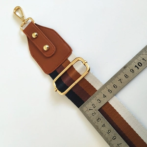 Close-up of 5cm wide navy and brown striped bag strap with gold metal hooks and leather end