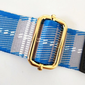 Close-up of adjustable blue plaid woven bag strap with polished gold metal buckle