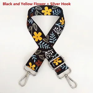Detail of adjustable black woven bag strap with yellow floral patterns and silver hooks