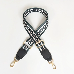 Detail of adjustable wide canvas bag strap with green chain pattern and gold buckles