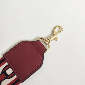 Detail of burgundy leather strap end with polished gold swivel hook and tricolor webbing