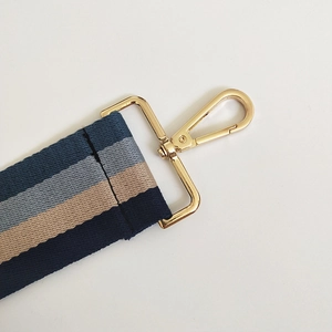 Detail of adjustable striped canvas bag strap with golden metal lobster clasps