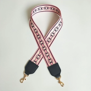 Detail of pink and white jacquard wide bag strap with black chain pattern and gold metal hooks