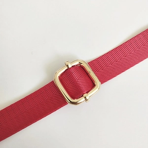Detail of red nylon woven shoulder strap with adjustable gold rectangular metal buckle