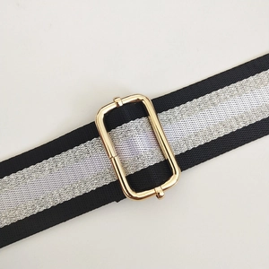 Detail of adjustable black strap with silver stripes and light gold metal buckle