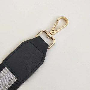Close-up of black and silver striped bag strap with gold lobster clasp and leather trim