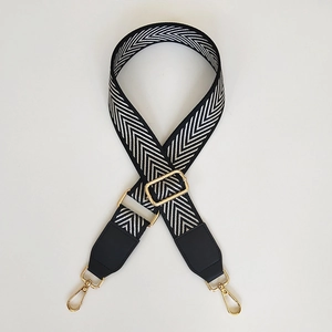 Detail of adjustable black and white herringbone woven strap with golden metal swivel hooks
