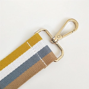 Detail of colorful striped woven strap with gold metal lobster clasp and white stitching