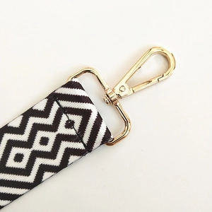 Detail of black and white geometric canvas bag strap with golden metal lobster clasps