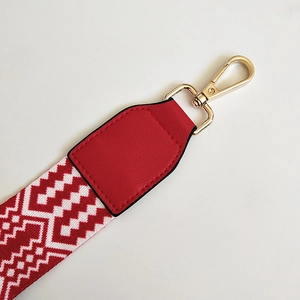 Close-up of red and white ethnic woven bag strap with golden lobster clasp and leather joint