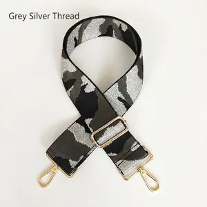 Macro shot of grey camouflage bag strap with silver thread weave and gold hardware