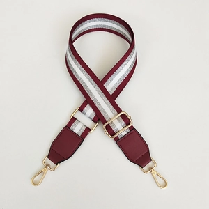 Detail van gestreepte bordeauxrode tasriem met zilverdraad en gouden metalen haken