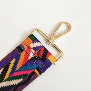 Close-up of geometric woven shoulder strap with gold metal lobster clasp and reinforced stitching