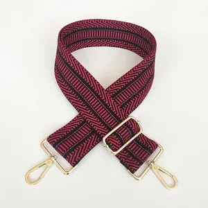 Detail eines Taschenriemens mit rot-schwarzem Fischgrätmuster und goldenen Metallschnallen