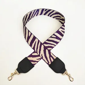 Detail of wide zebra pattern bag strap in purple and cream with gold metal hooks