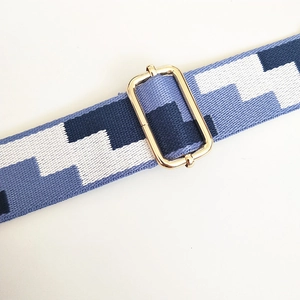 Close-up of embroidered wide bag strap with blue geometric patterns and gold metal buckle