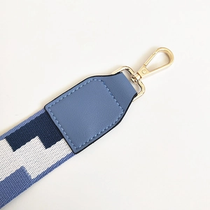 Detail of blue geometric embroidered bag strap with golden metal swivel hooks and leather ends