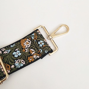 Detail of floral embroidery on wide bag strap with gold-tone metal lobster clasp