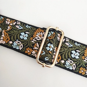 Detail of floral embroidery on wide bag strap with light gold metal adjustment buckle