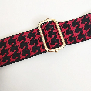 Close-up of red and black geometric woven strap with adjustable gold metal buckle