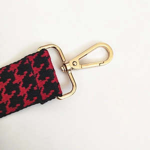 Detail of red and black houndstooth pattern bag strap with polished gold lobster clasp